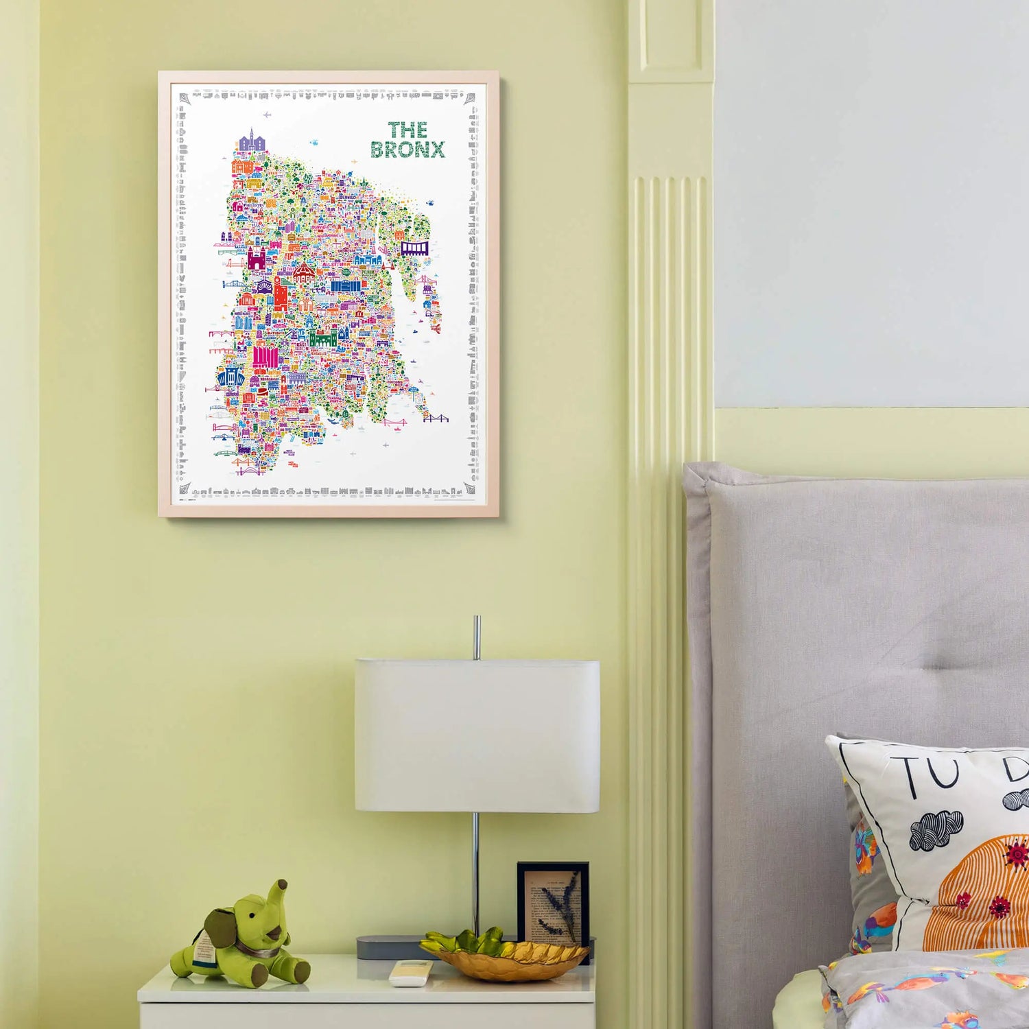 Colorful map of The Bronx on a wall above a nightstand with a lamp and decorative items.