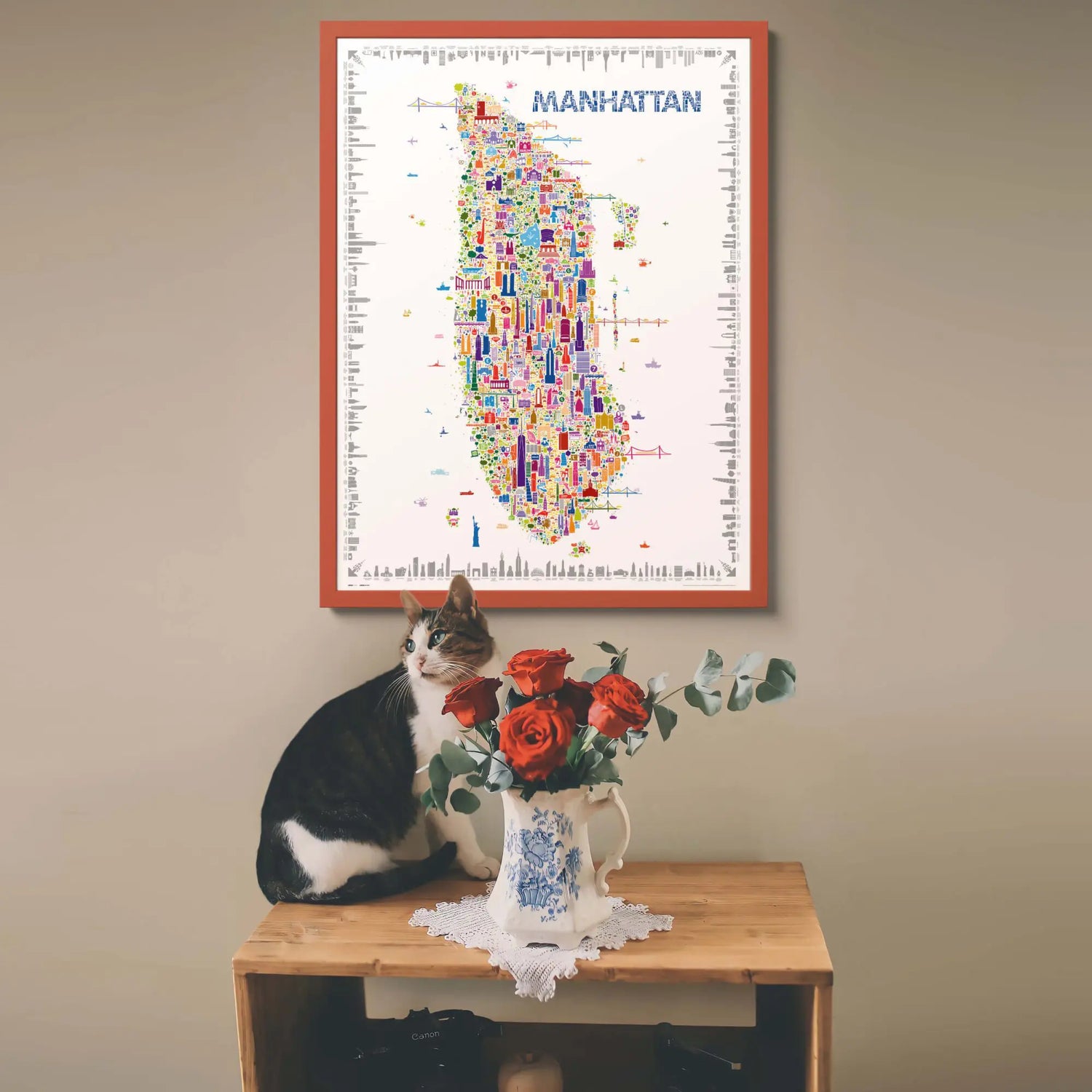 Cat sitting on a table with flowers, framed map of Manhattan above