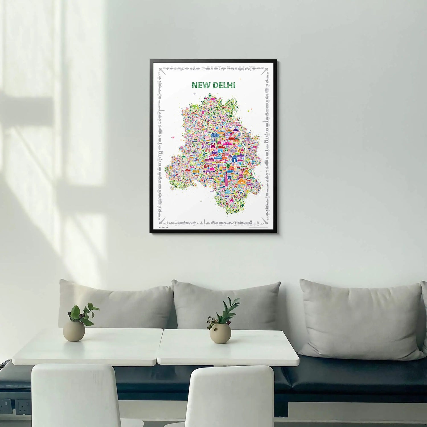 Framed map of New Delhi on a wall above a white sofa with a small table and plants.
