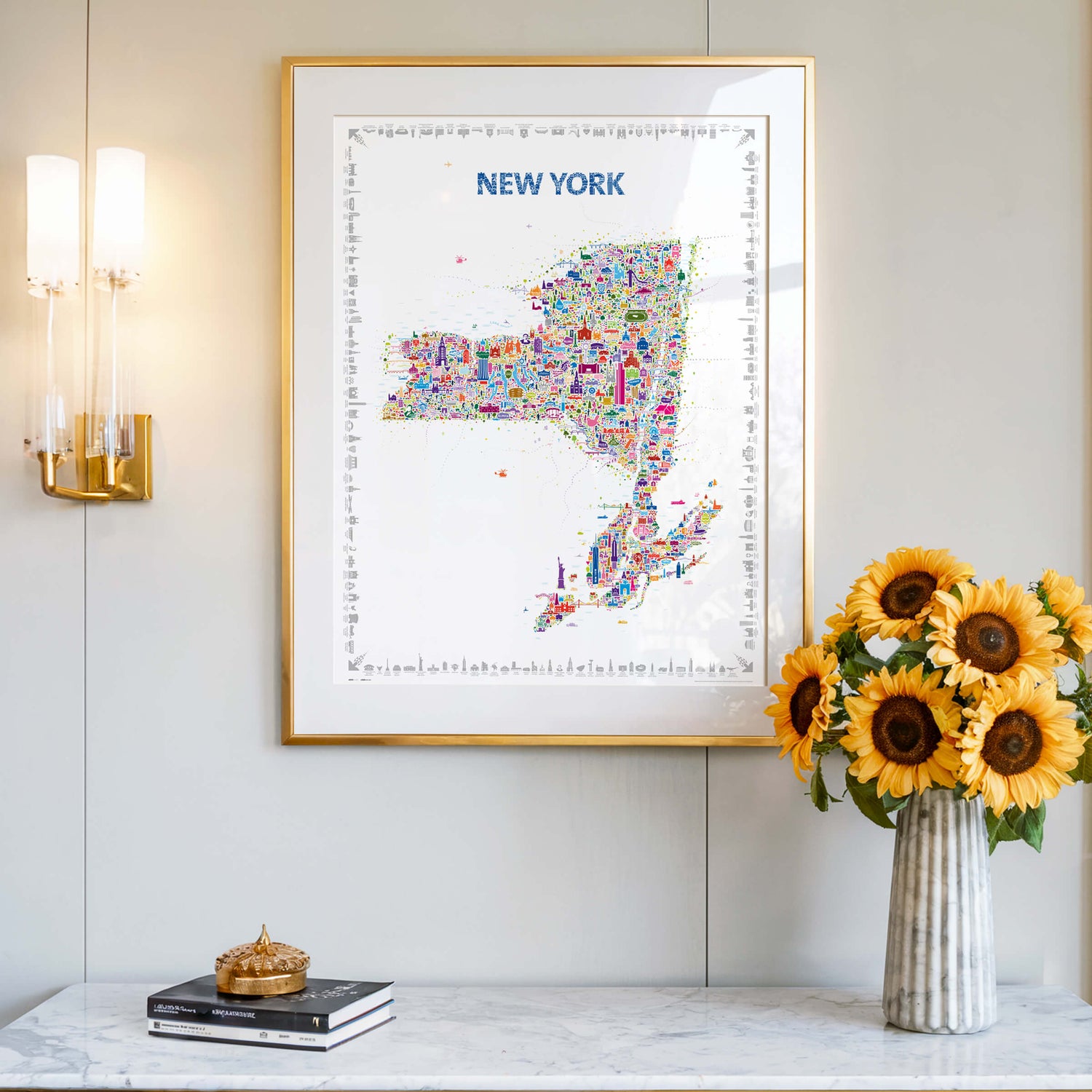 Colorful New York State illustrated map poster in a gold frame displayed above a marble console with sunflowers in a modern interior.