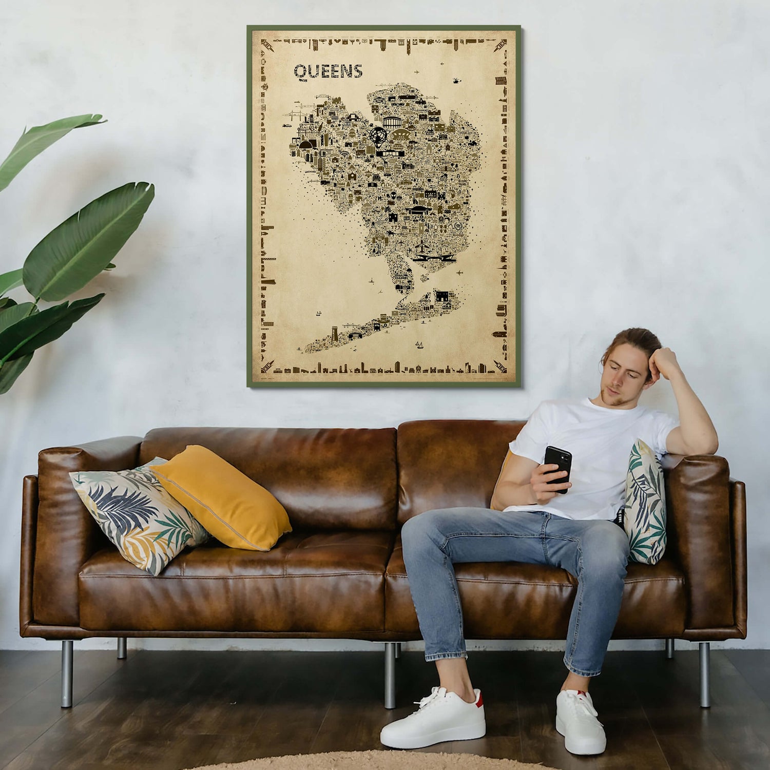 Iconic Queens Poster – Antique Edition in a wooden frame above a brown leather sofa. NYC borough map art in sepia tones styled in a warm, vintage-inspired living room.