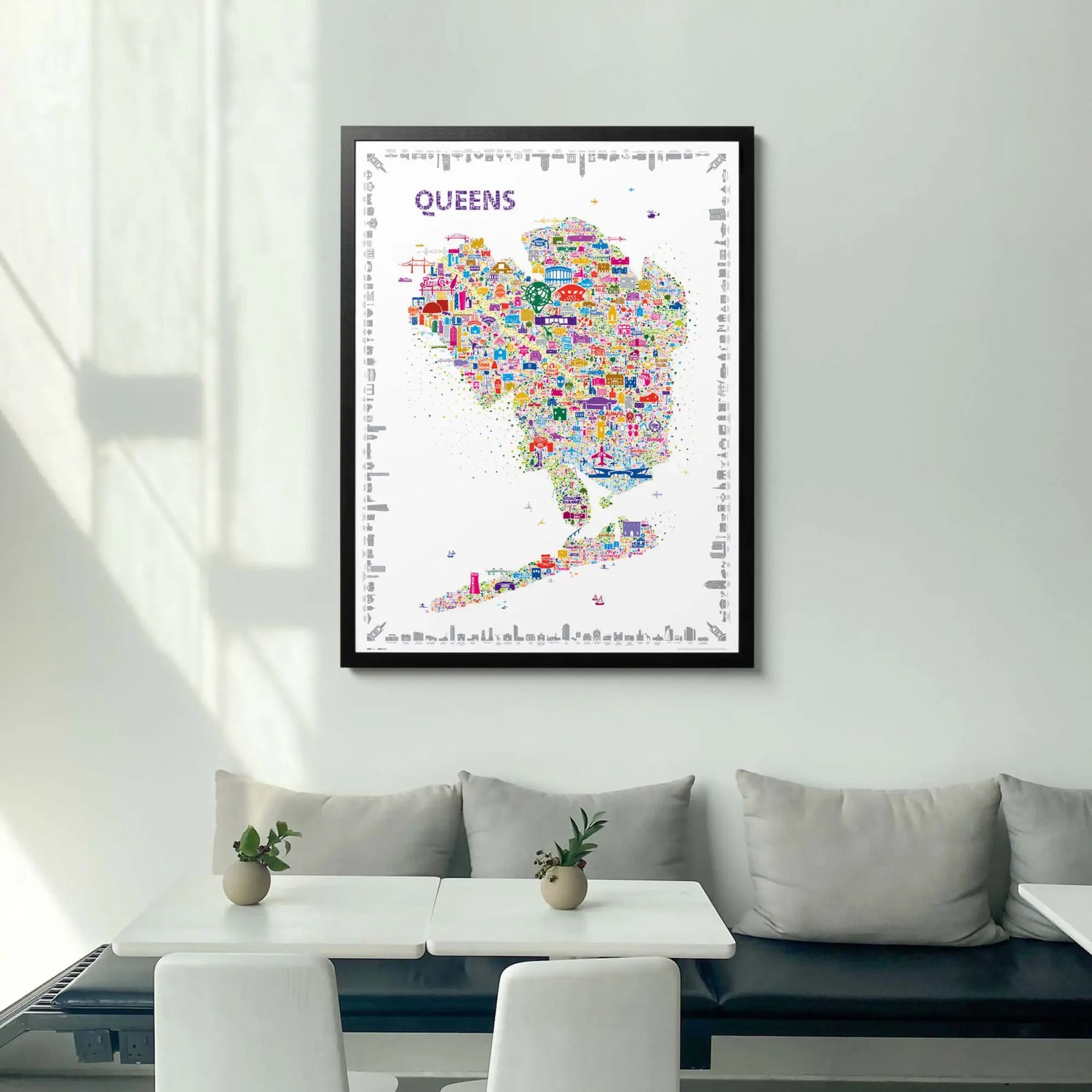Framed Alfalfa New York Queens illustrated map poster hanging on a light gray wall above a modern dining nook with neutral seating and minimalist decor.