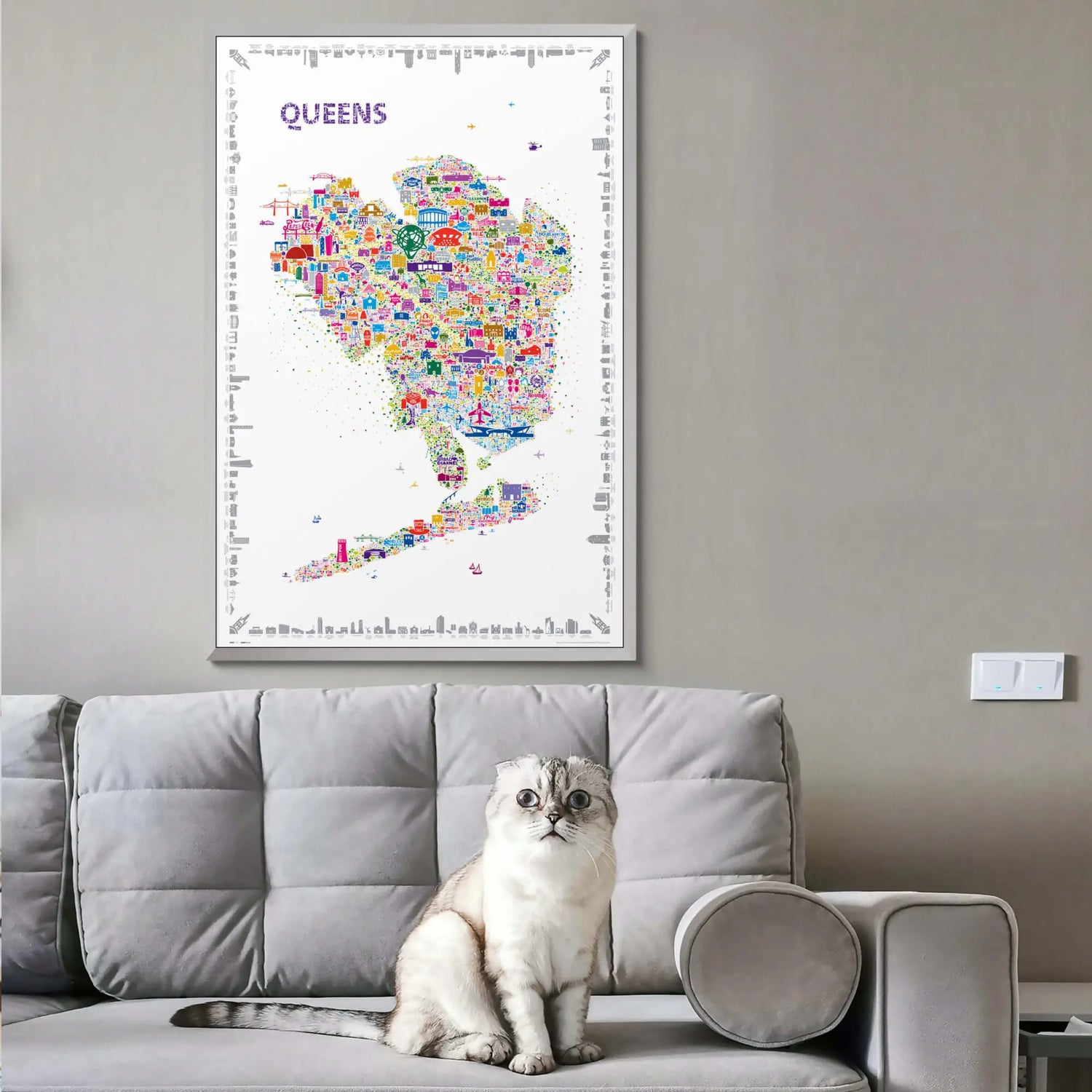 Framed Alfalfa New York Queens illustrated map poster hanging above a modern gray sofa with a white cat sitting in a cozy living room.