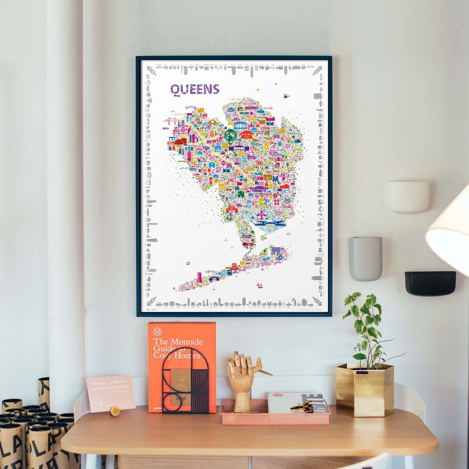 Framed map of Queens on a wall above a desk with decor items.
