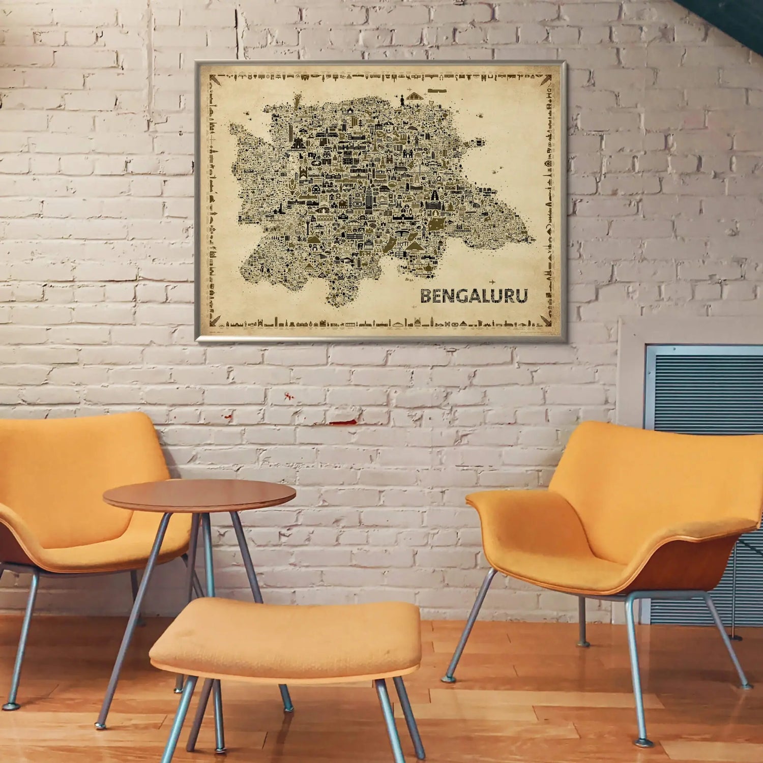 Framed map of Bengaluru on a brick wall with orange chairs and a small table below.