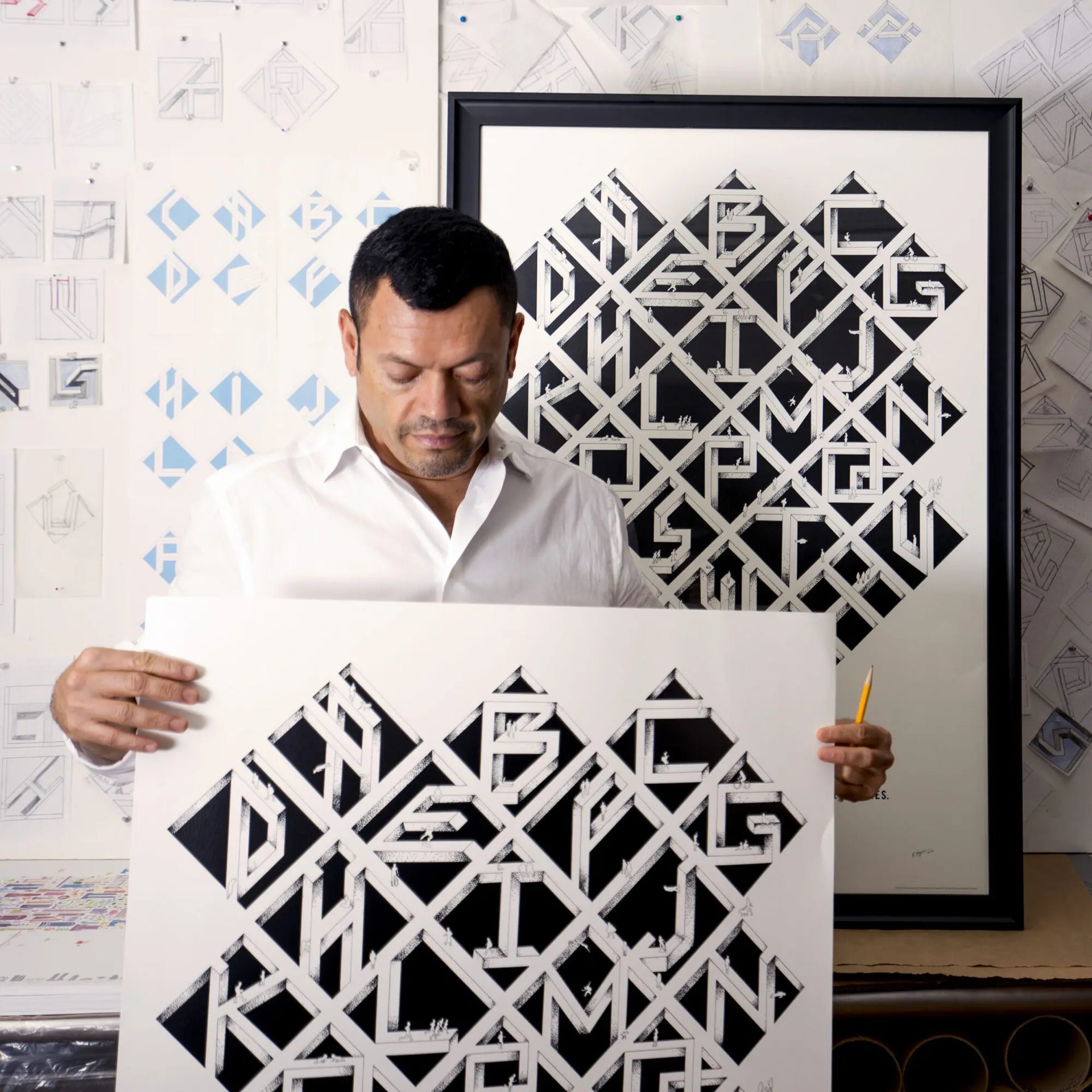 Man holding two black and white geometric art pieces in a room with artistic decor.