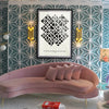 Alfalfabet typographic poster in black frame displayed above pink velvet curved sofa with gold wall sconces on geometric teal wallpaper