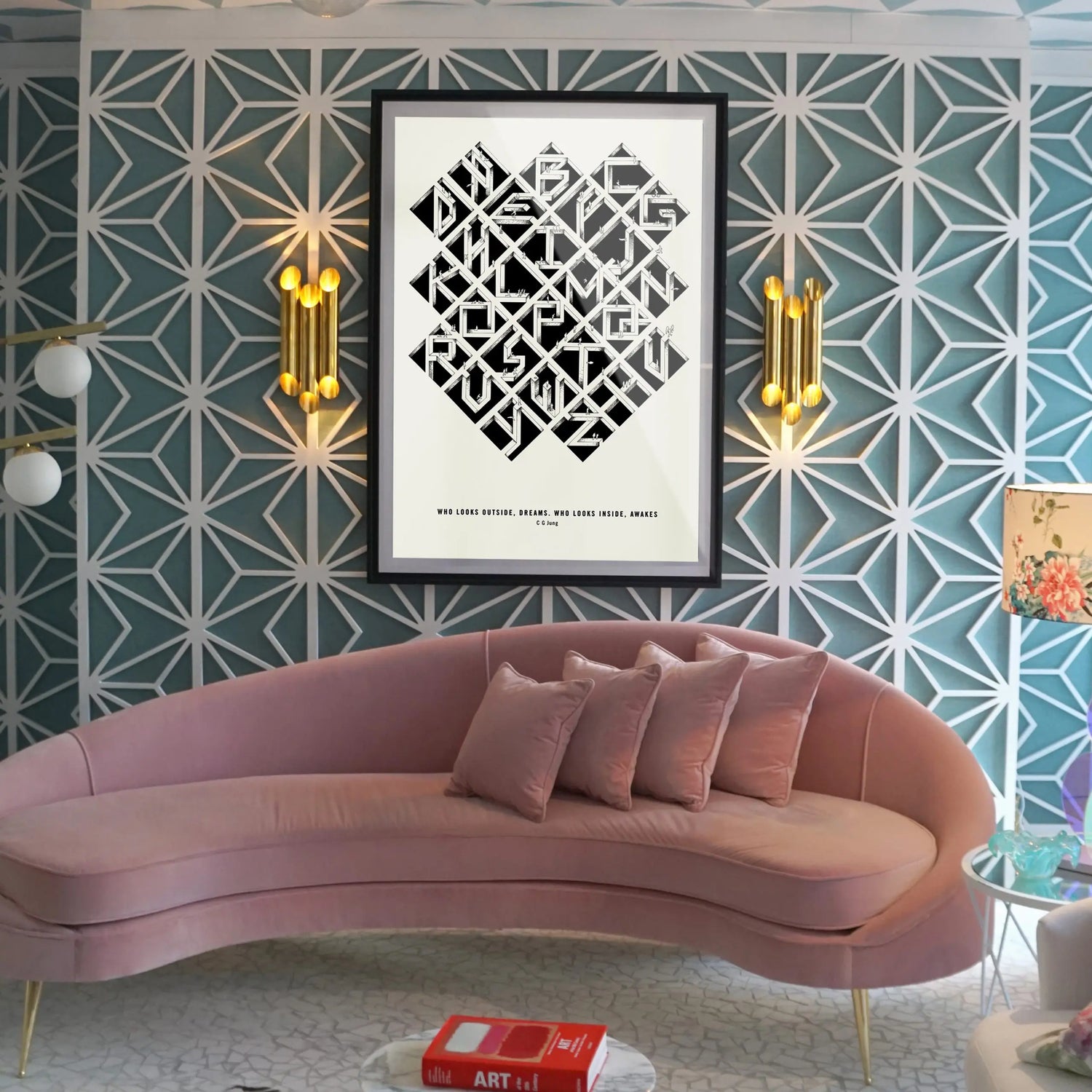 Alfalfabet typographic poster in black frame displayed above pink velvet curved sofa with gold wall sconces on geometric teal wallpaper