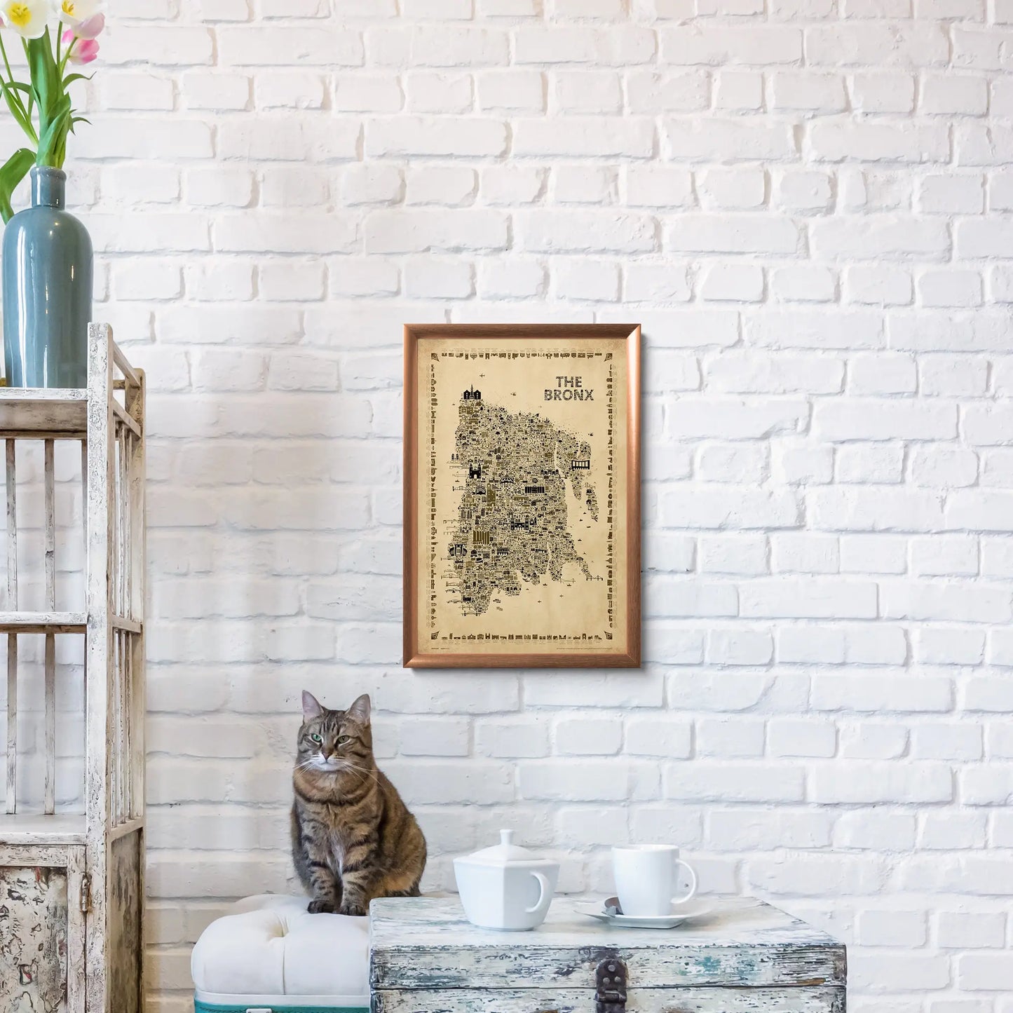 Cat sitting on a table with a framed map of Brora on a white brick wall.