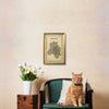Cat sitting on a chair with a map of New Delhi framed above, next to a potted plant.