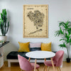 Iconic Queens antique map poster in wooden frame displayed above modern seating area with pink chairs, yellow cushions and indoor plants