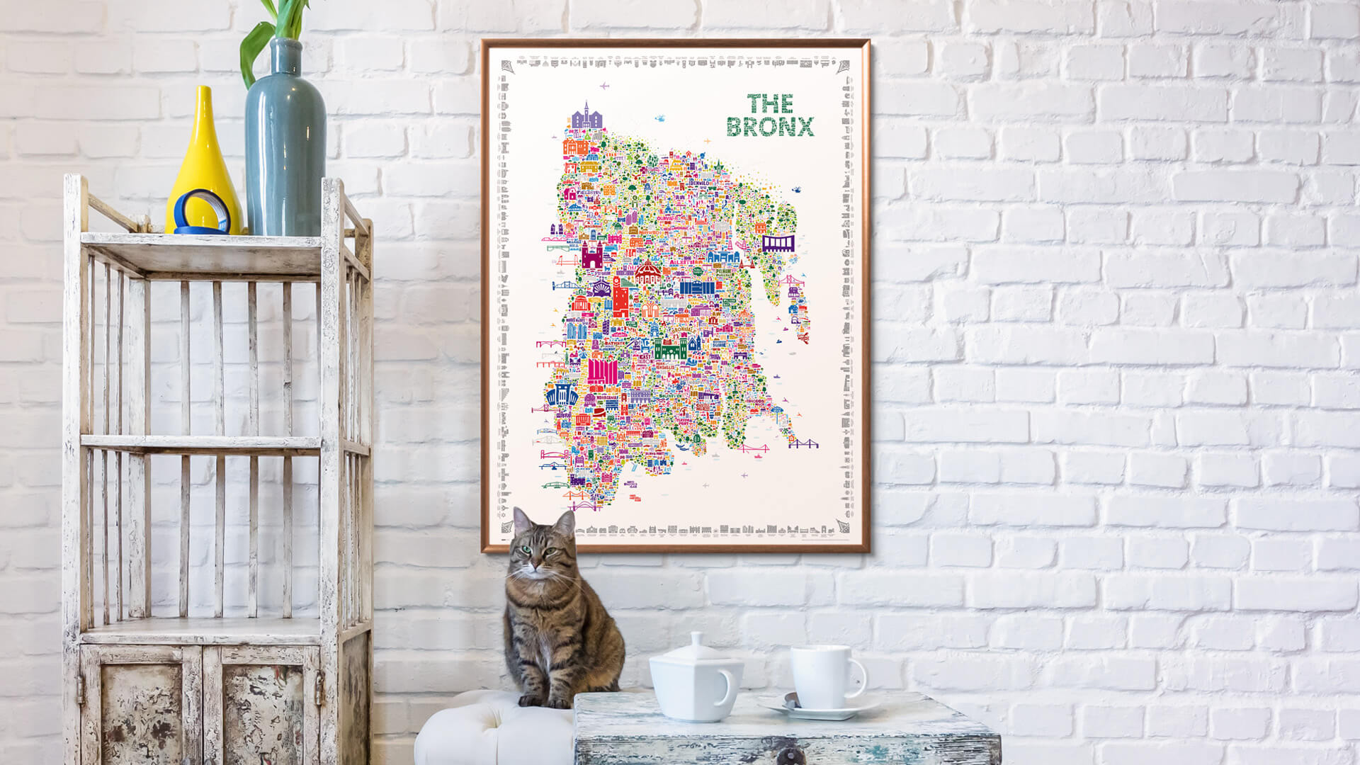 Framed map of The Bronx on a white brick wall with a cat sitting on a table below.