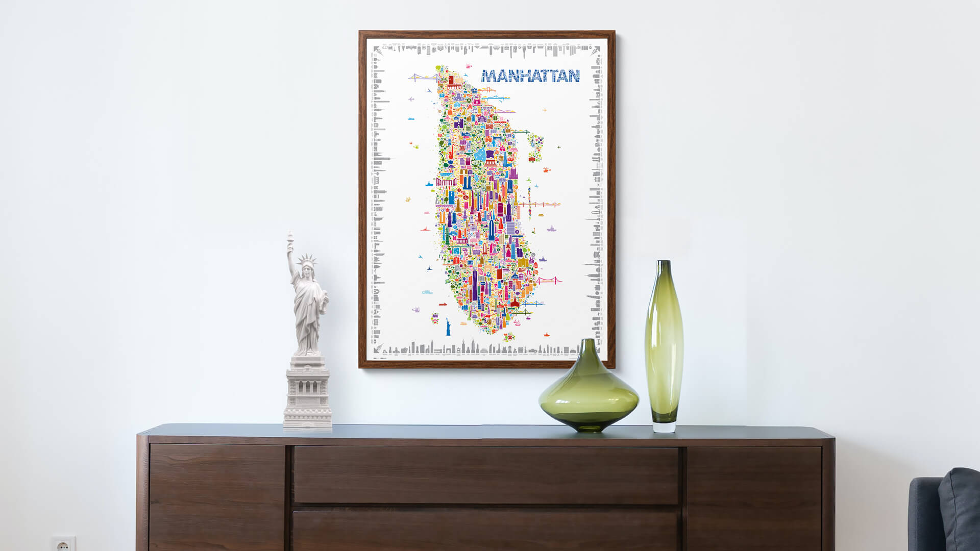 Iconic Manhattan colorful illustrated map poster in dark wood frame displayed above modern credenza with Statue of Liberty figurine and green glass vases