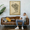 Iconic Queens antique map poster in gold frame displayed above brown leather sofa with person relaxing showing size and living room placement