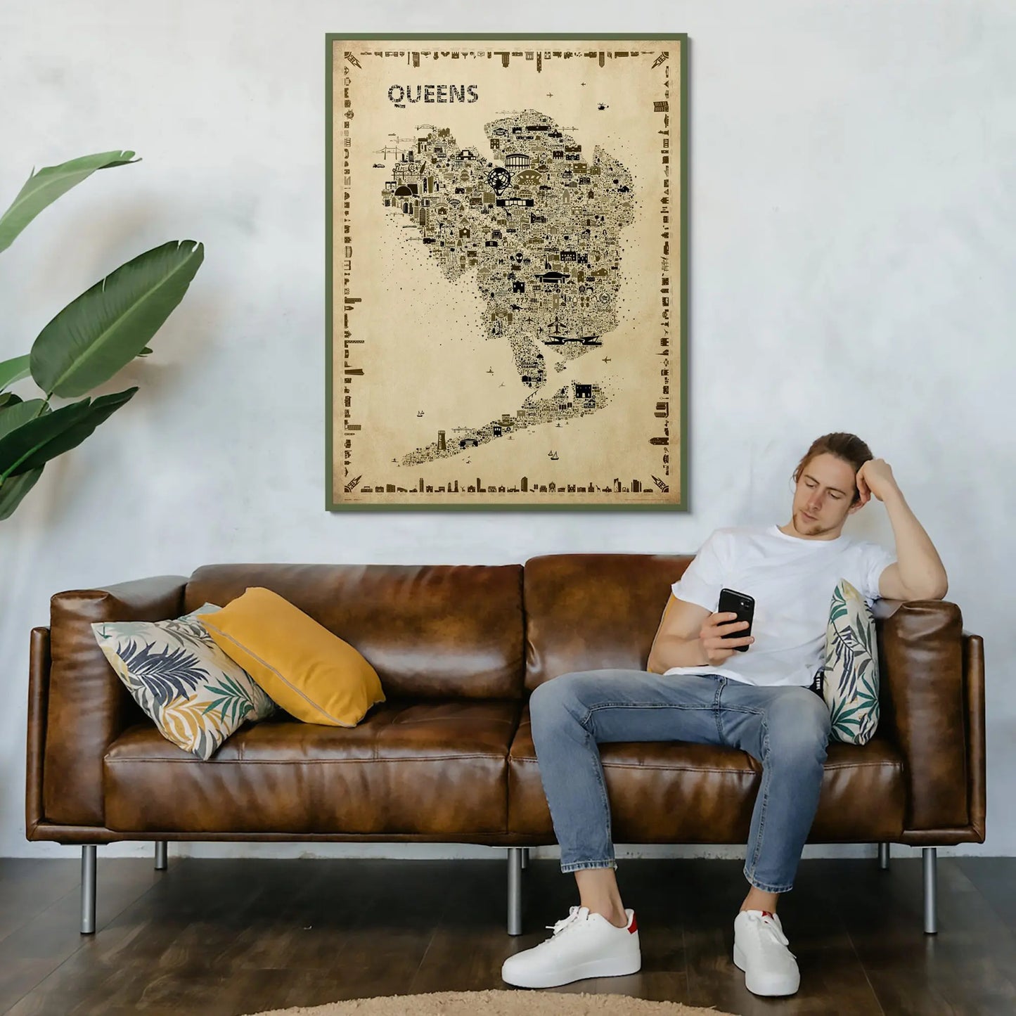 Iconic Queens antique map poster in gold frame displayed above brown leather sofa with person relaxing showing size and living room placement