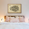Bedroom with a map of Paris on the wall above a bed with pink and white pillows.