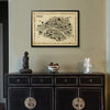 Framed map of Paris above a dark wooden cabinet with decorative items.