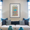 Central Park illustrated map art print framed in black, displayed above a modern cream sofa with blue and patterned cushions — stylish wall decor by Alfalfa New York.