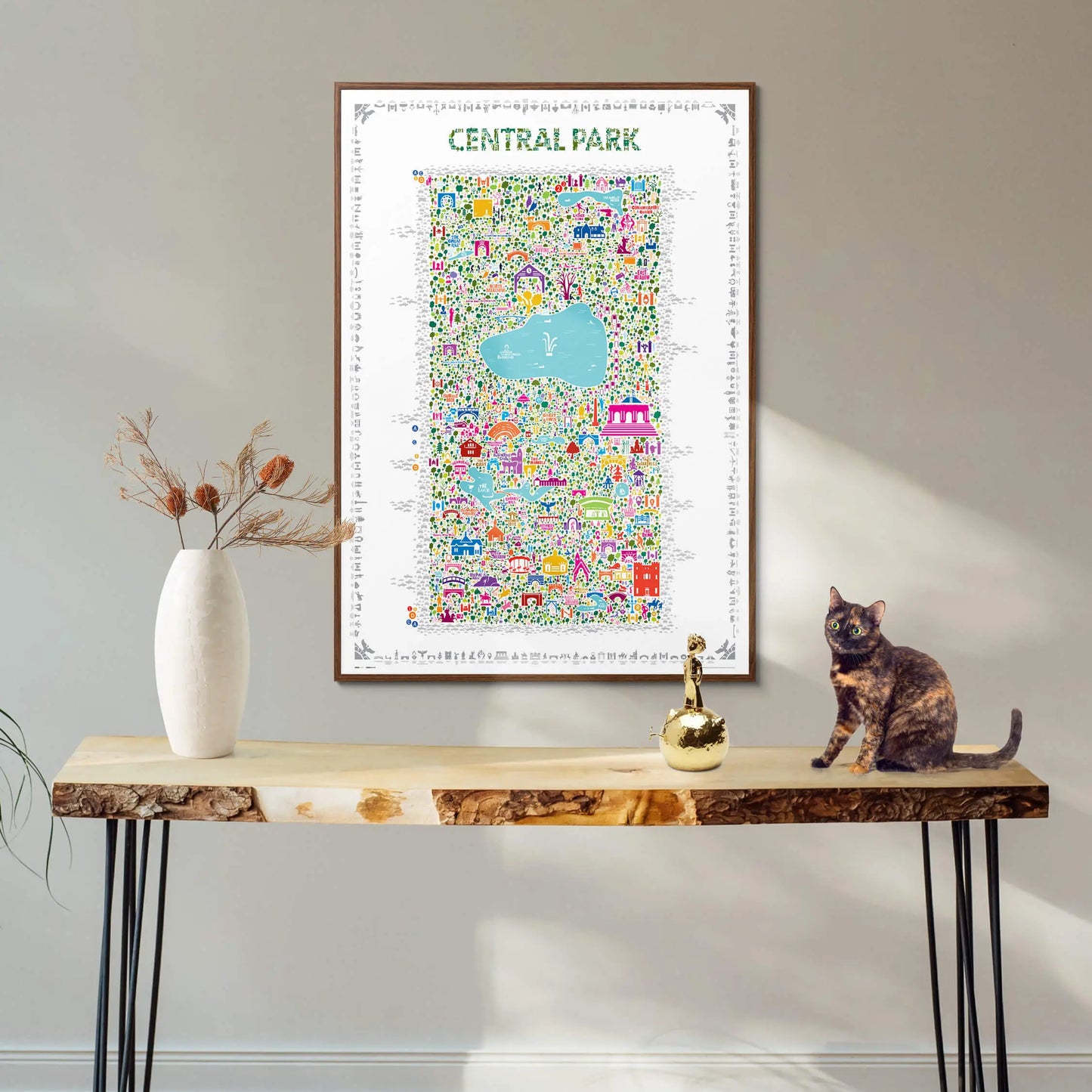 Framed Central Park illustrated map art print displayed above a modern console table with decorative vase and cat — minimalist interior styling by Alfalfa New York.