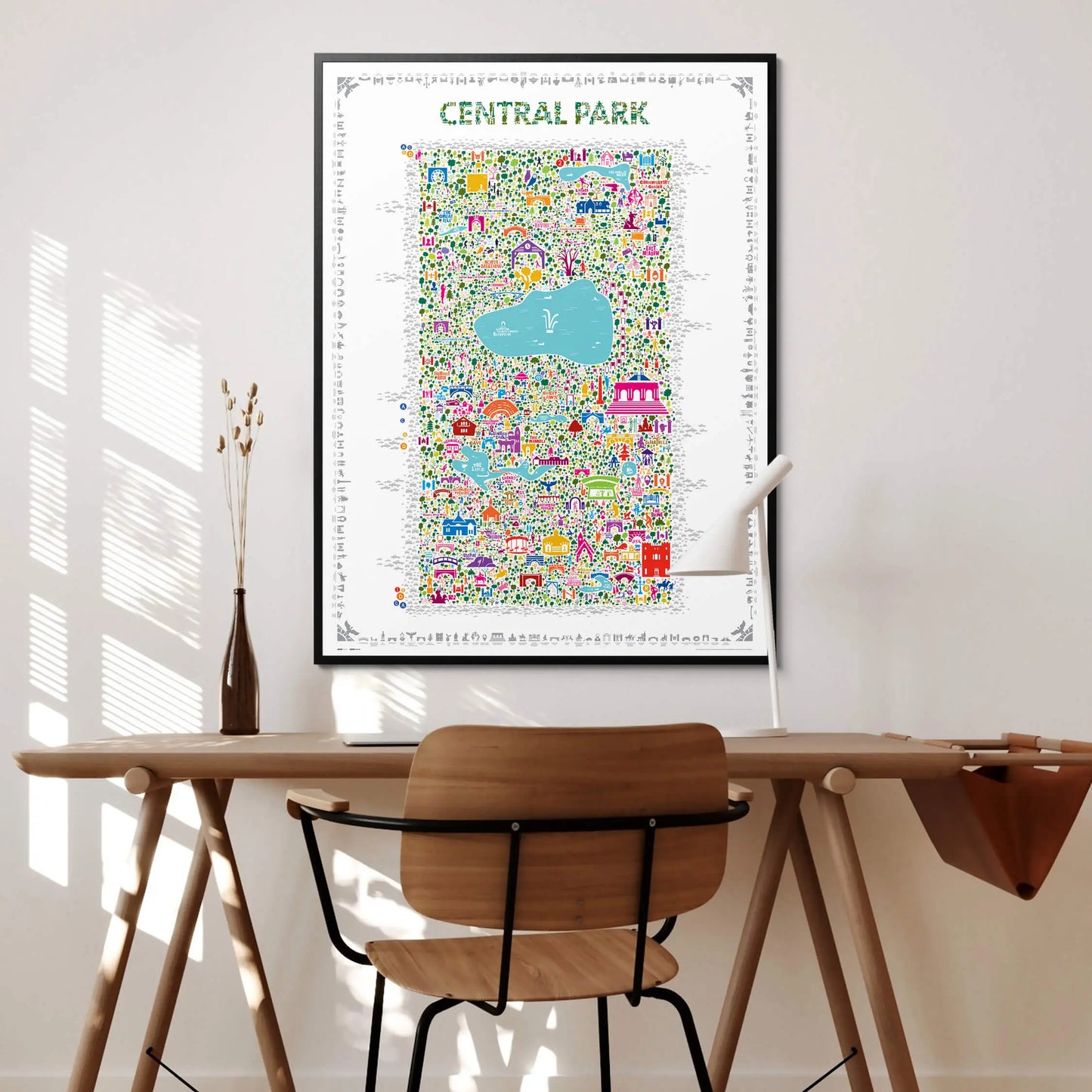 Central Park illustrated map art print in black frame displayed above a wooden desk with a chair and vase — modern home office wall decor by Alfalfa New York.