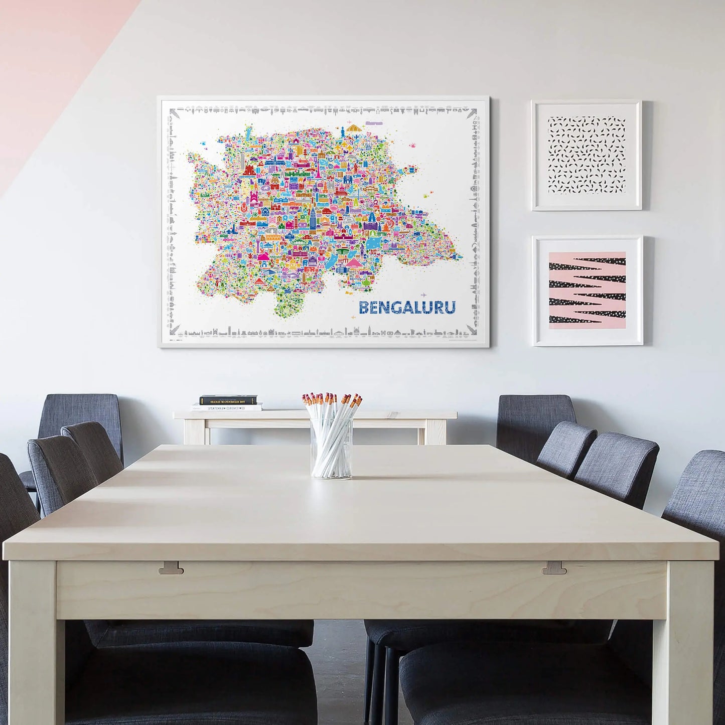Vibrant Bengaluru city map art print framed on a white wall above a modern dining table with gray chairs, adding a colorful and artistic touch to the minimalist interior.