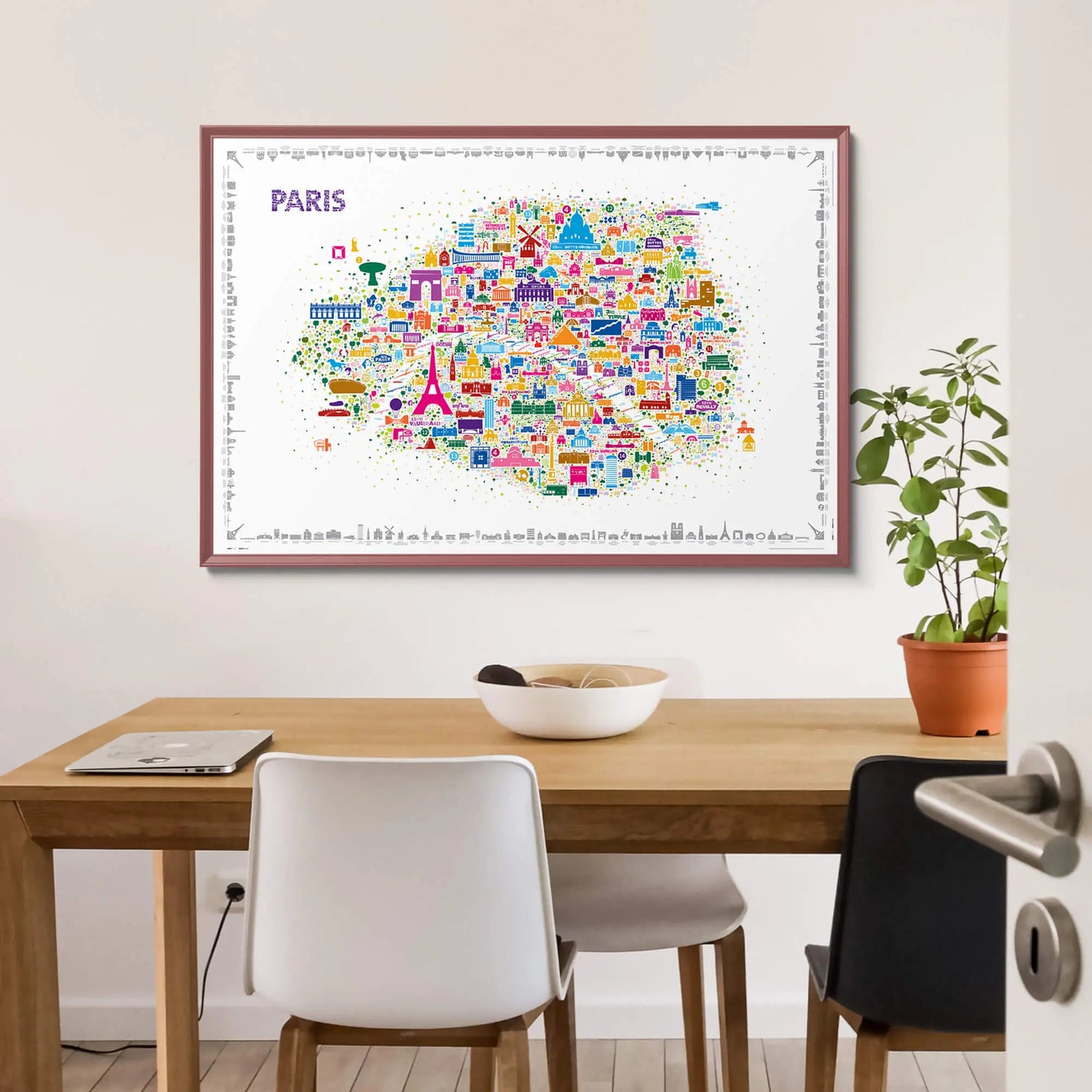Iconic Paris colorful illustrated map poster in burgundy frame displayed above light wood dining table with white chairs and terracotta plant