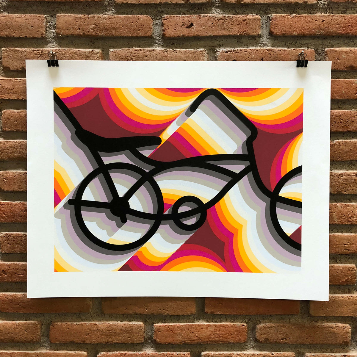 East LA Lowrider Bike, an unframed screenprint on white paper with wide margins, hung from two black clips on a brick wall