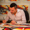 Rafael Esquer signing a copy of East LA Lowrider Bike in pencil, with more prints pinned to the wall behind him
