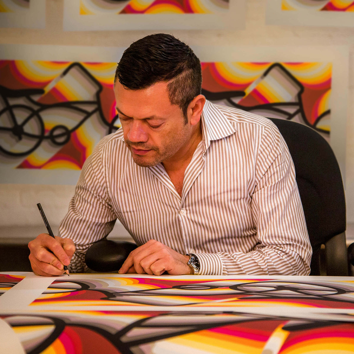 Rafael Esquer signing a copy of East LA Lowrider Bike in pencil, with more prints pinned to the wall behind him