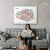 Woman working on laptop on gray sofa beneath colorful Paris illustrated map poster in green frame with modern living room decor