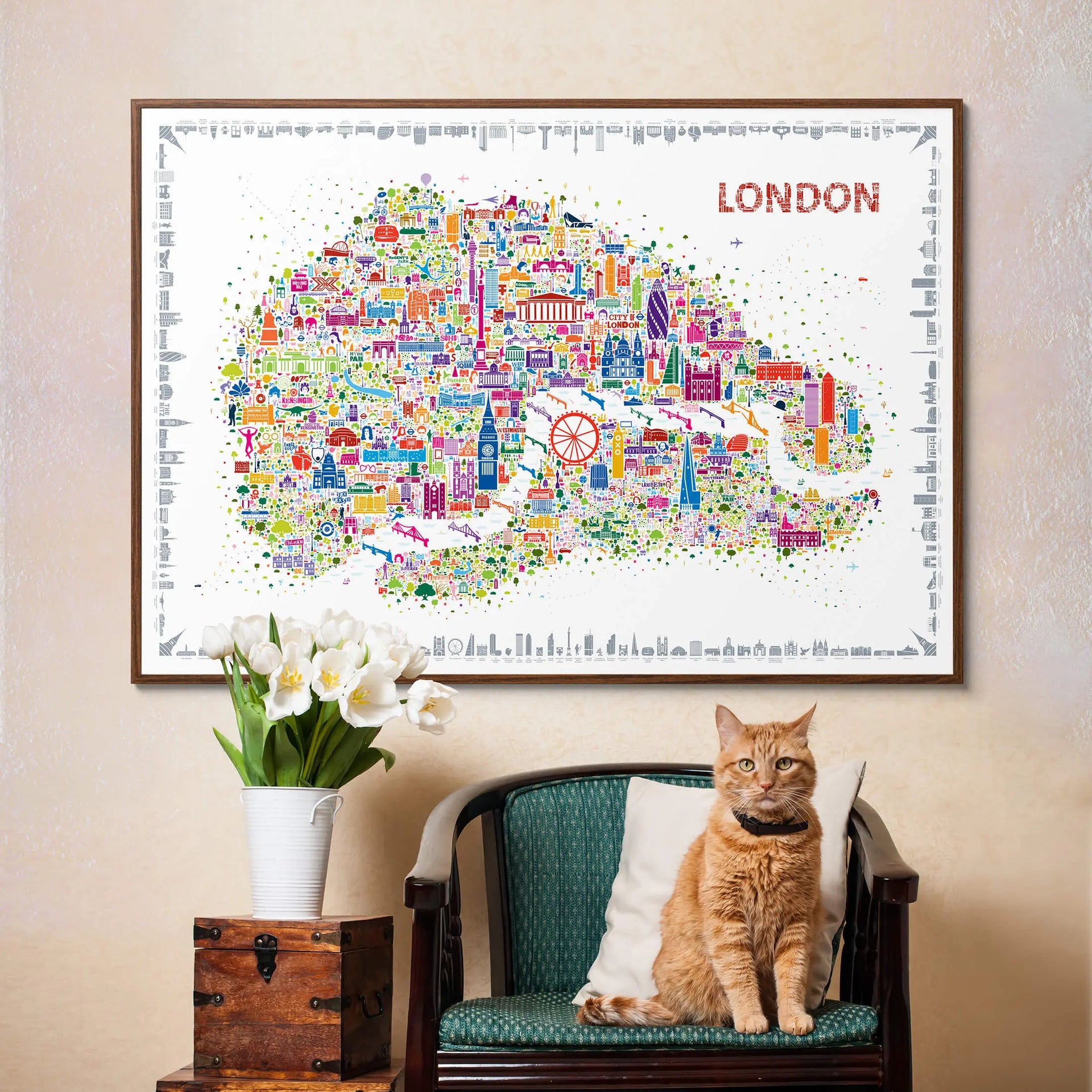 Framed map of London with colorful icons, a cat sitting on a chair below, and a vase with flowers to the left.