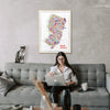 Framed New Jersey city map art print in natural wood displayed above a modern grey sofa — stylish home wall decor by Alfalfa New York.
