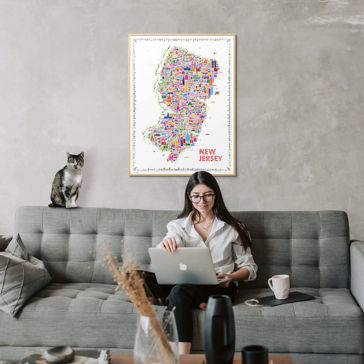 Framed New Jersey city map art print in natural wood displayed above a modern grey sofa — stylish home wall decor by Alfalfa New York.