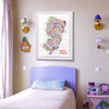 Colorful New Jersey city map art print framed in white wood, displayed above a cozy children’s bedroom setup — playful modern wall art by Alfalfa New York.