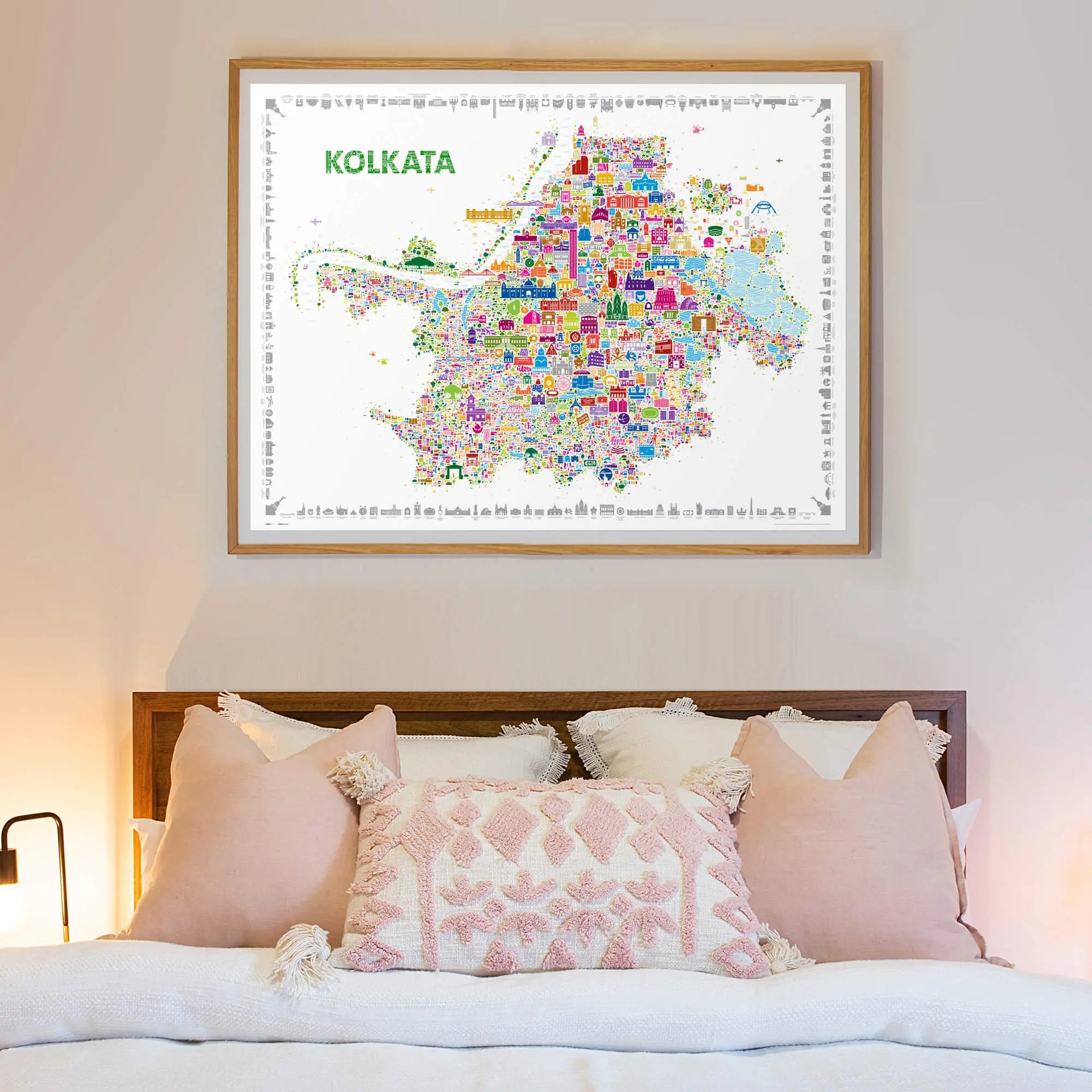Framed map of Kolkata on a wall above a bed with pink pillows.
