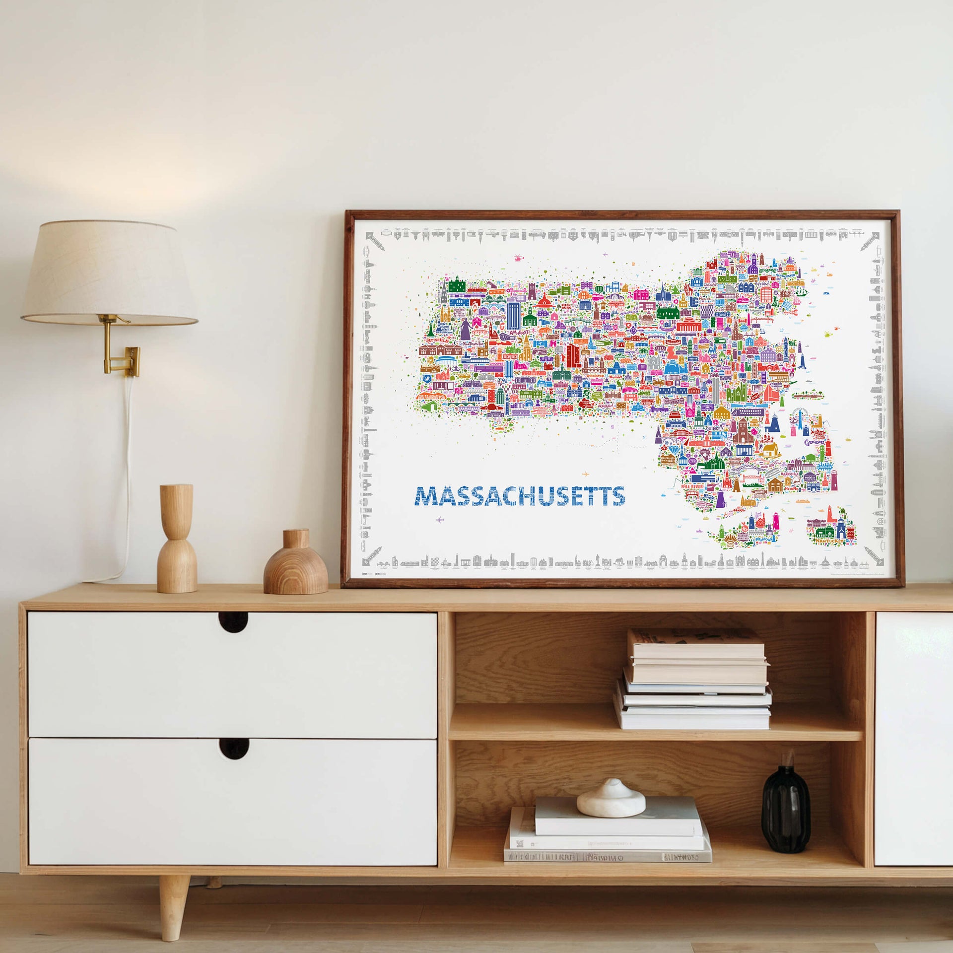 Colorful illustrated Massachusetts map poster displayed as modern wall art above a mid-century cabinet, featuring hundreds of hand-drawn icons of Boston, Cape Cod, and New England landmarks. Contemporary travel map artwork and designer home décor print by Alfalfa New York.