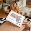 Framed colorful Massachusetts illustrated map poster being held, showing hundreds of icons representing Boston, Cape Cod, and New England landmarks. A contemporary travel map wall art print and designer home décor artwork.