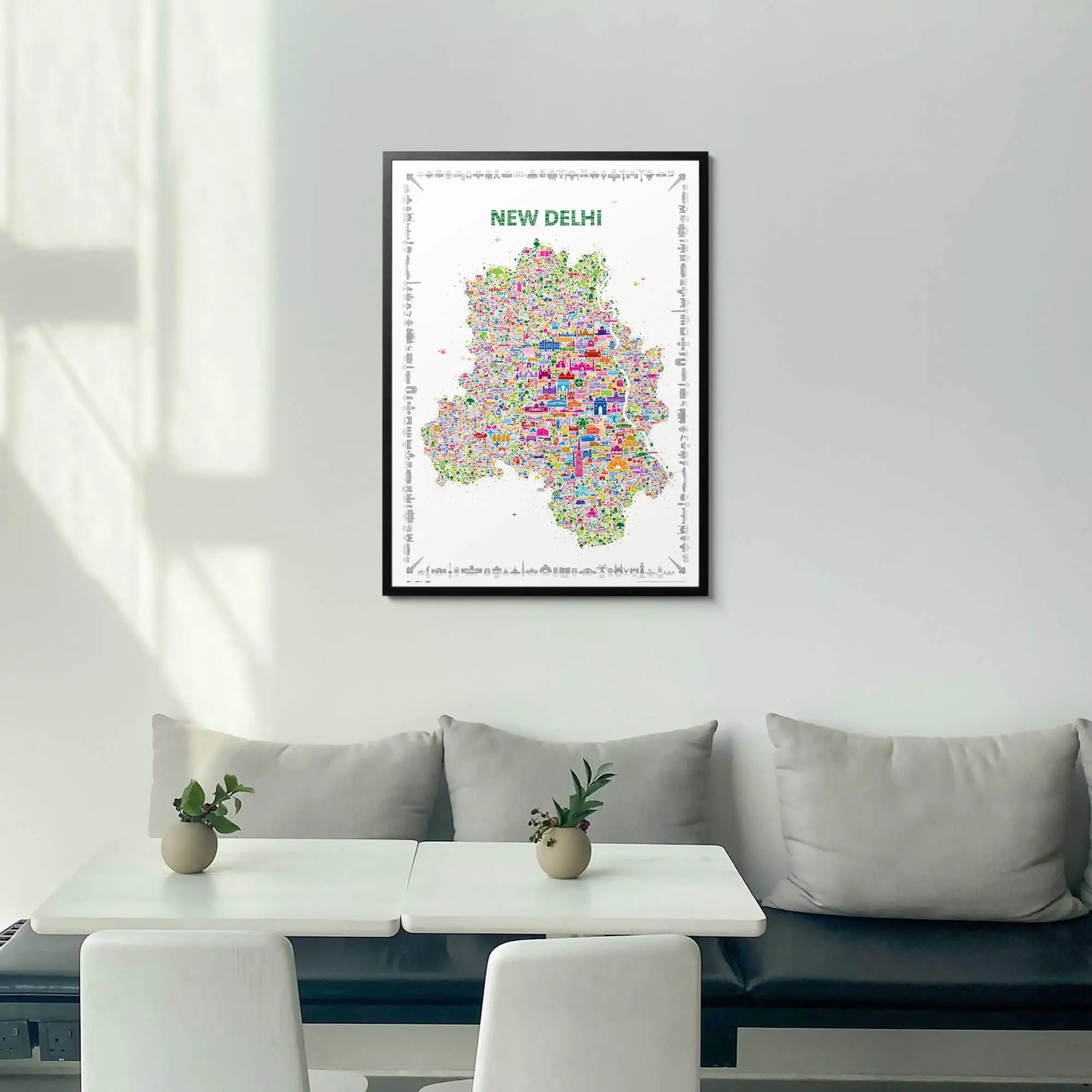 Framed map of New Delhi on a wall above a white sofa with a small table and plants.