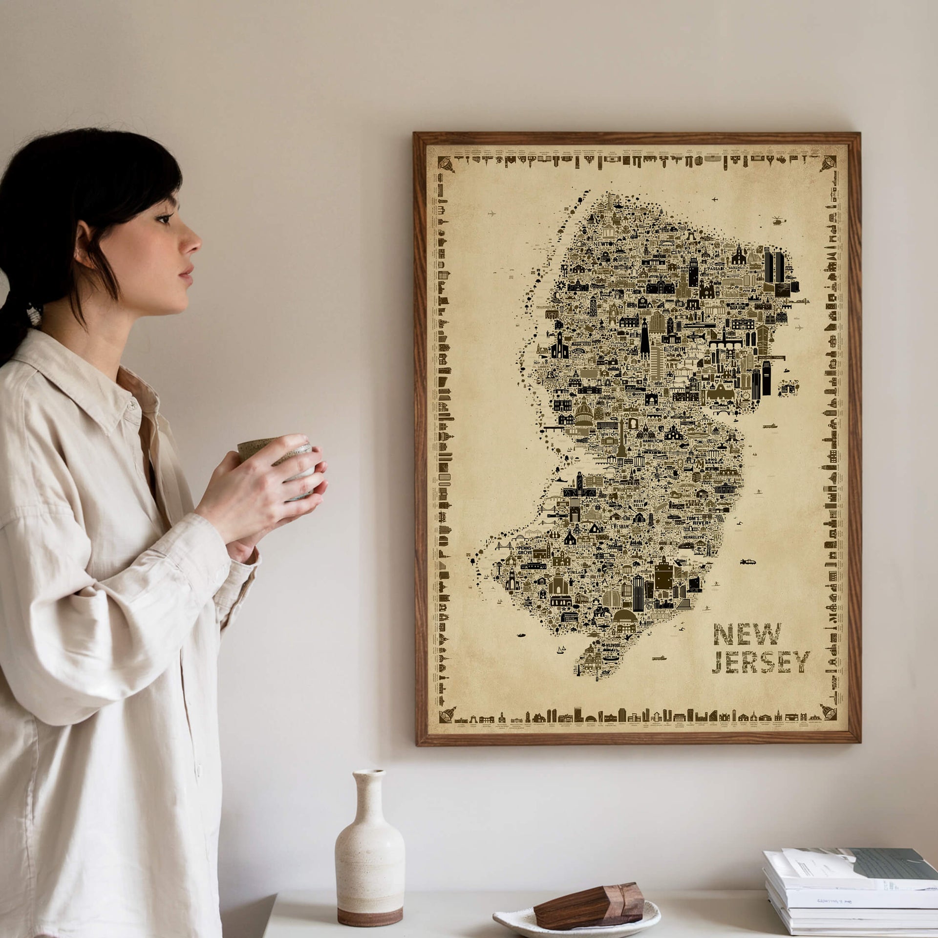 Woman admiring the Iconic New Jersey Antique Edition vintage map poster in a natural wood frame. Elegant old-world wall art filled with hand-drawn landmarks, architecture, and hidden details celebrating the Garden State.
