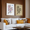 Colorful and Antique New York City Five Boroughs illustrated map posters displayed side by side in natural wood frames above a white sofa with mustard pillows in a warm modern living room.