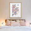Framed map of New York on a wall above a bed with decorative pillows.