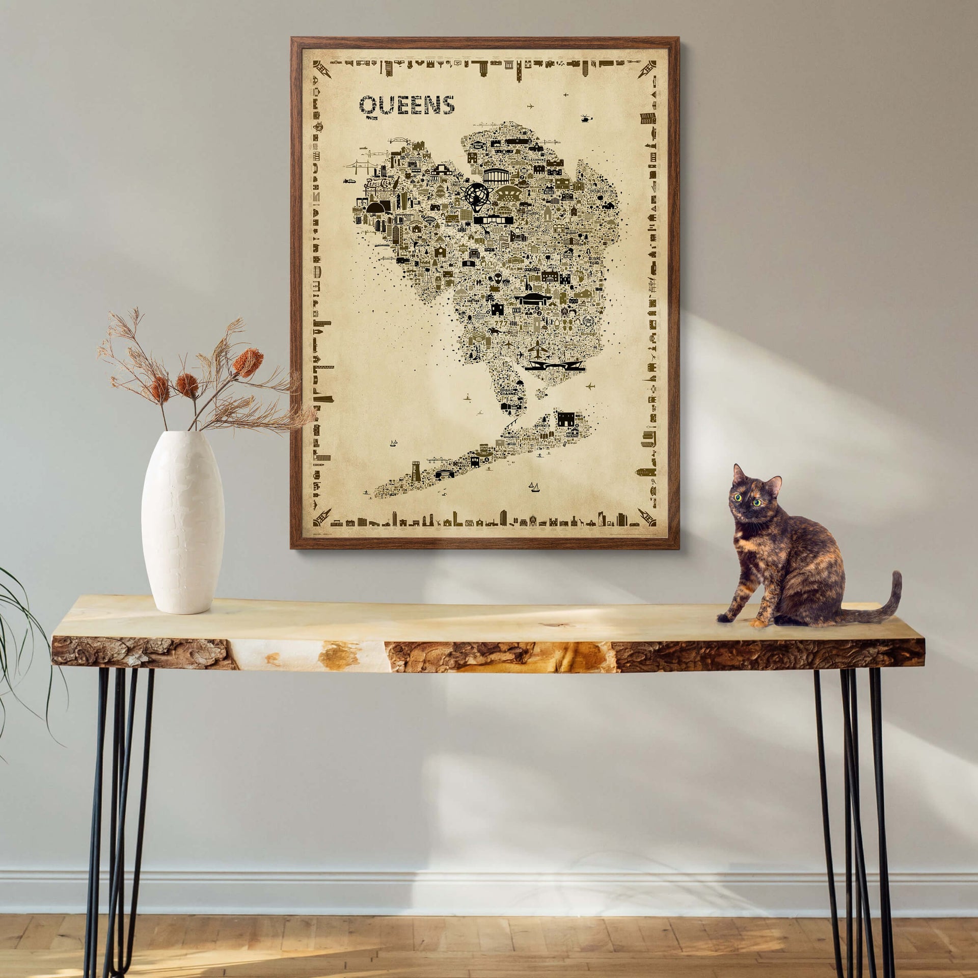 Framed Queens Antique Poster in a dark gallery-style wood frame above a rustic table with a turtle-shell cat and dried flowers in a ceramic vase. Artistic NYC map artwork for timeless interiors.