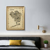 Antique-style Queens map poster framed in gold above a gray headboard in a chic bedroom with velvet yellow and white pillows, a modern gold wall lamp, and houseplant. Warm, historical wall art with NYC flair.
