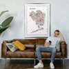Man sitting on a brown leather sofa in a living room with a colorful map of Queens above him.