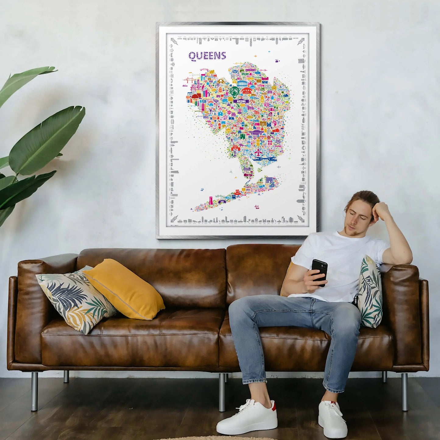 Man sitting on a brown leather sofa in a living room with a colorful map of Queens above him.
