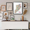 Wall with framed pictures and a map of Staten Island above a white cabinet with decorative items.