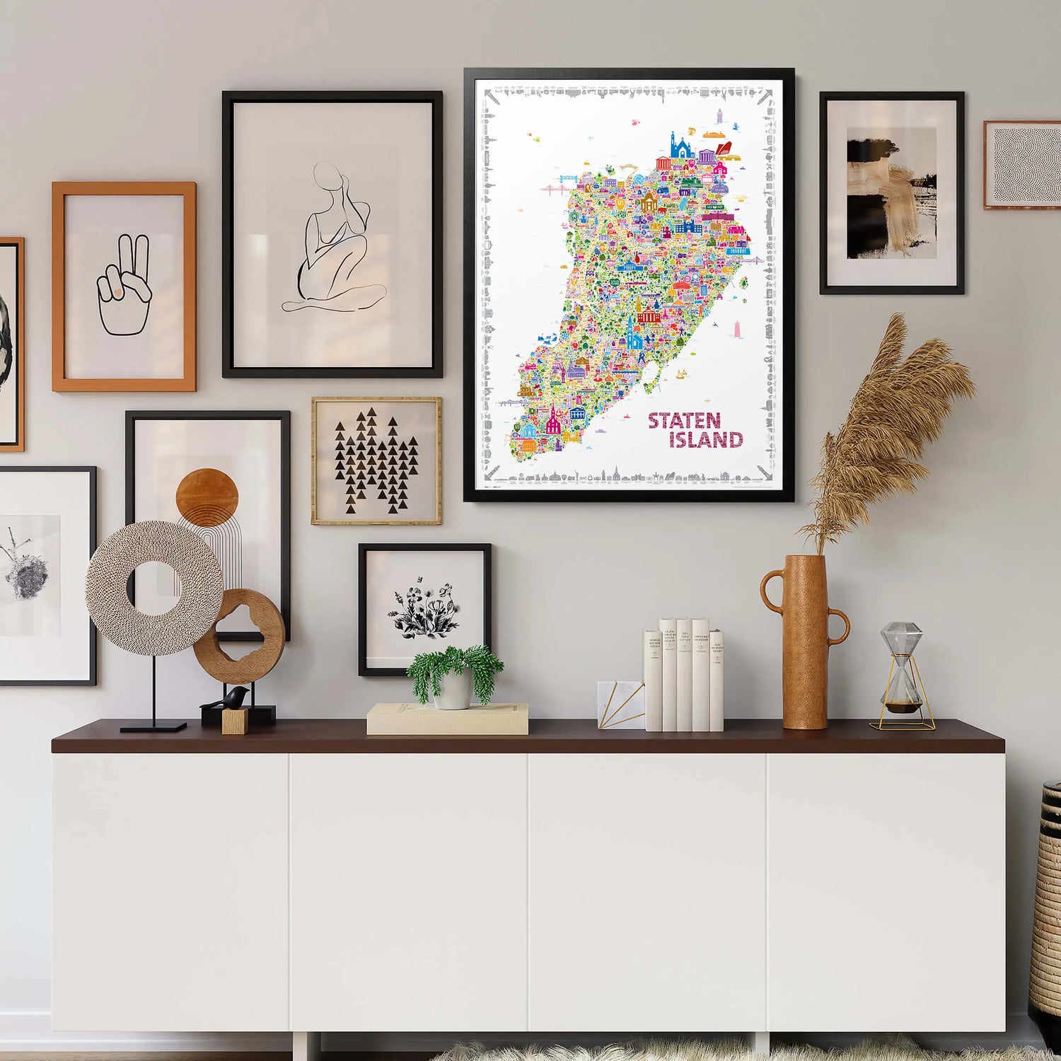 Wall with framed pictures and a map of Staten Island above a white cabinet with decorative items.