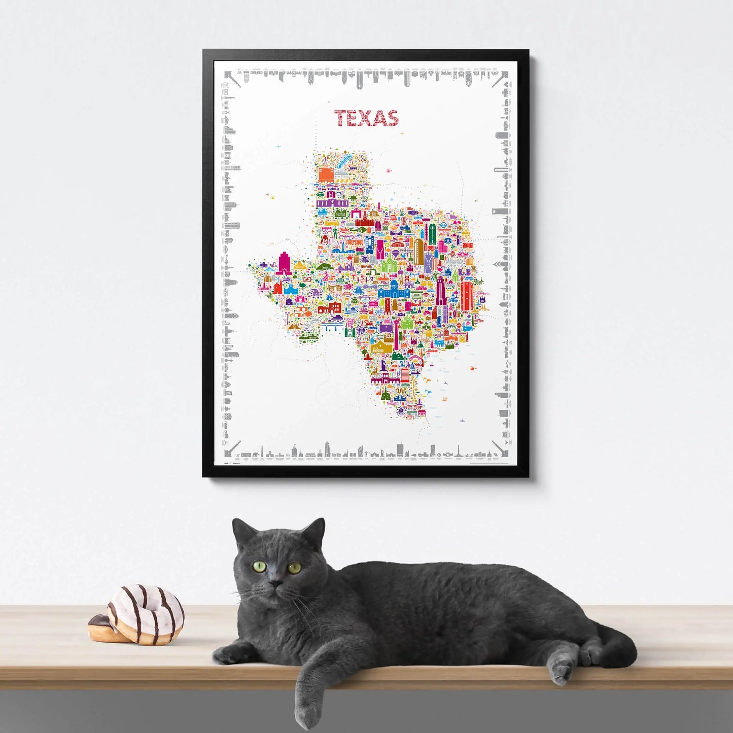 Framed map of Texas with colorful icons, a cat lying on a surface below.