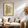 Framed The Bronx Antique illustrated map poster hanging above a cream sofa in a warm sunlit living room with textured white walls, wicker accents, and neutral decor.