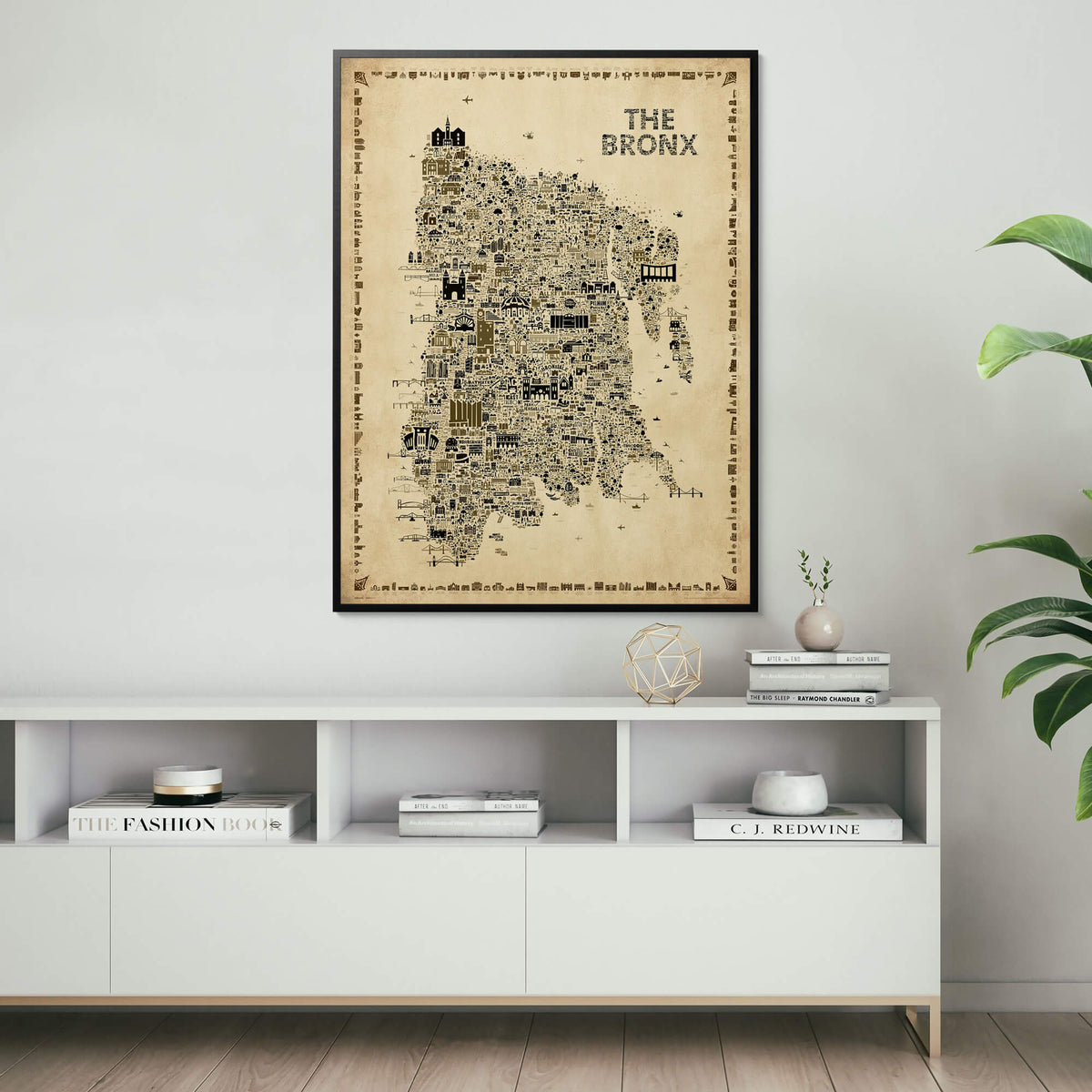 Framed The Bronx Antique illustrated map poster displayed above a modern white console cabinet with books, sculptural decor, a ceramic vase, and green houseplants.